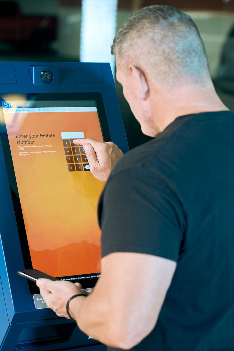 A man interacts with a touch-screen kiosk to enter a mobile number.